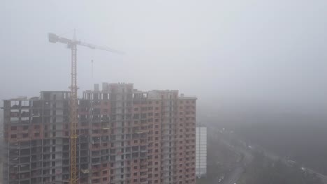 Aerial-view.-A-multi-storey-brick-house-in-the-city-in-a-fog.-A-construction-crane-is-installed-on-the-site-of-the-construction-of-a-residential-building.-New-homes-for-sale-and-rent-of-real-estate