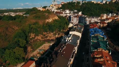 Zángano-de-la-cámara-se-mueve-bajo-techos-de-edificios-en-antigua-europeas-callejuelas-con-casas-de-colores-y-los-peatones-al-atardecer-4K