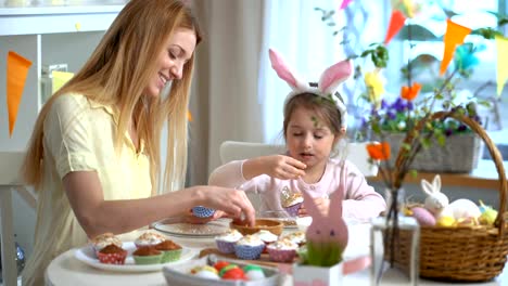 Joven-madre-y-su-pequeña-hija-con-orejas-de-conejo-divertidos-cocinar-cupcakes-de-Pascua