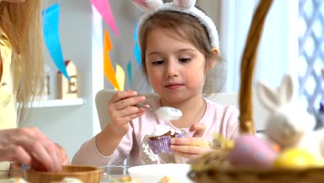 Joven-madre-y-su-hija-con-orejas-de-conejo-cocinar-cupcakes-de-Pascua