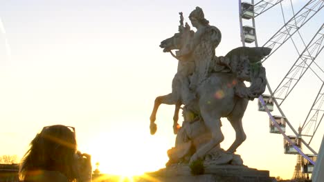 Turista-tomando-foto-de-estatua-ecuestre-de-Pegasus-y-rueda-grande,-puesta-de-sol