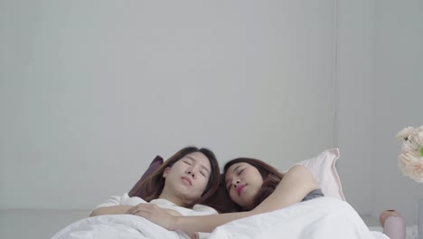 Asian-women-lesbian-happy-couple-waking-up-in-morning.-Asian-girls-sitting-on-bed-stretching-in-cozy-bedroom-at-home.-Funny-women-friends-after-wake-up.-LGBT-Lesbian-couple-together-indoors-concept.