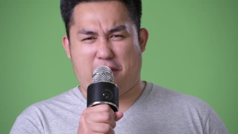 Young-handsome-overweight-Asian-man-against-green-background