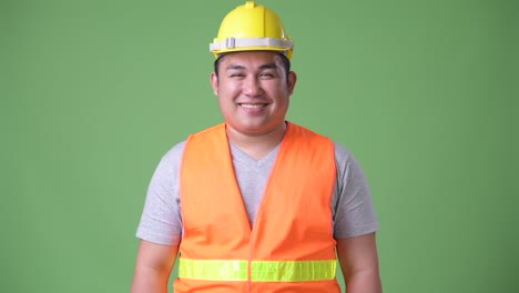 Young-handsome-overweight-Asian-man-construction-worker-against-green-background