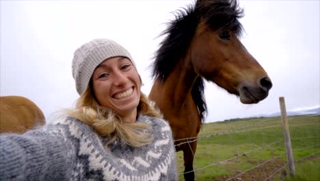 Blondes-Haar-Mädchen-in-Island-unter-Selfie-Porträt-mit-Islandpferd-in-grüne-Wiese.-Im-Frühling,-Bewölkter-Himmel,-Frau-trägt-isländischen-grau-wolle-Pullover-gedreht.-Die-Leute-reisen-tierischen-Zuneigung-Konzept-Zeitlupe