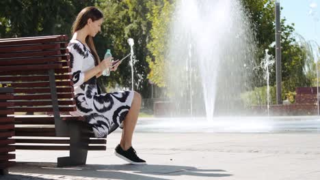 mujer-de-negocios-joven-sentado-en-un-banco-de-agua-y-trabajar-en-la-tableta