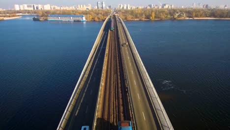 Antenne,-Top-Aussicht-von-Drone:-Metro-Zug-fährt-über-eine-Brücke-mit-PKW-und-LKW.