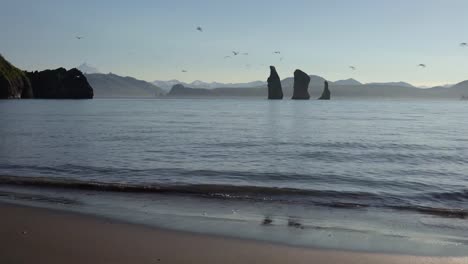 Rocky-islands-in-sea-and-beach-of-black-volcanic-sand-on-sunny-day