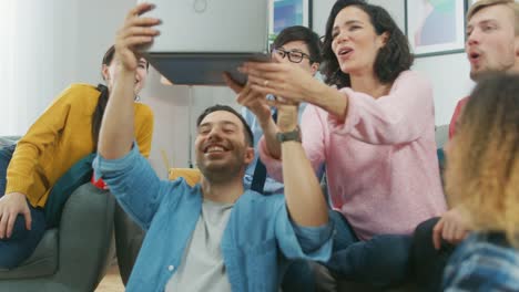 Diverse-Group-of-Friends-Use-Laptop-in-the-Living-Room.-Happy-Beautiful-Girls-and-Guys-Doing-Live-Streaming.-They-Have-Fun-and-Laugh.