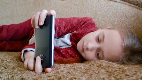 Girl-teenager-watching-a-video-in-the-phone-while-lying-on-the-couch.