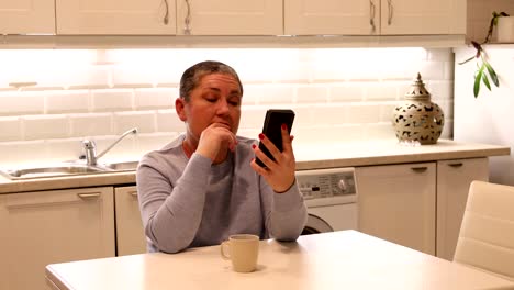 Mujer-con-pelo-corto-gris-usando-smartphone-en-la-cocina