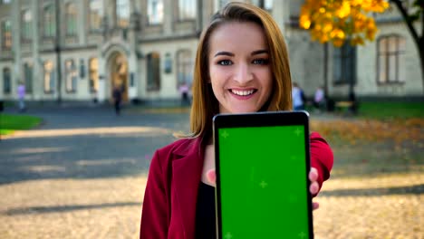 Young-attractive-female,-student-showing-screen-of-the-tablet-to-camera,-outside-the-university