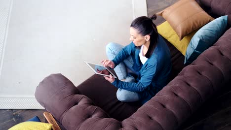 Top-view-smiling-hipster-young-woman-relaxing-on-couch-using-tablet-pc