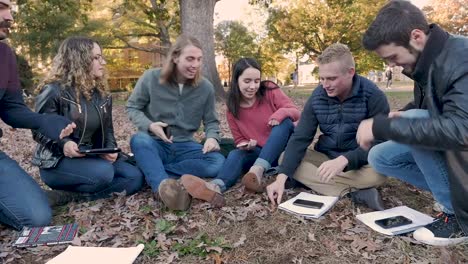 Amigos-de-la-Universidad-sentados-fuera-riendo-mientras-mantienen-la-tecnología-digital