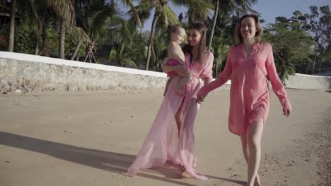 The-concept-of-the-strange-adventures-of-people.-Happy-lesbian-couple-with-babe-walking-on-beautiful-tropical-beach.-one-of-the-women-with-a-mustache-on-her-face-as-a-symbol-of-emancipation