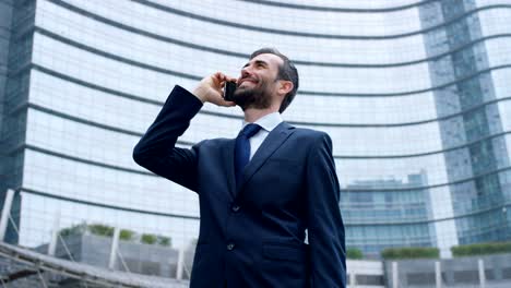 Un-hombre-de-negocios-contestar-el-teléfono,-enviar-mensajes-y-sonrisas-para-las-hermosas-noticias-de-trabajo-y-en-el-fondo-se-ve-a-un-pueblo.