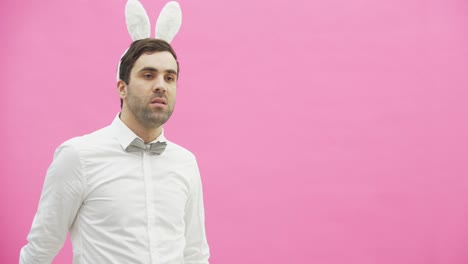 Young-handsome-boy-standing-on-a-pink-background.-A-man-with-rabble-ears-on-his-head.-A-man-holding-a-carrot-puts-it-in-his-mouth-and-reproduces-the-movements-of-a-cigarette-with-a-cigarette-lighter.