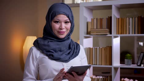 Closeup-shoot-of-adult-muslim-businesswoman-using-the-tablet-looking-at-camera-and-smiling-happily-on-the-workplace-indoors