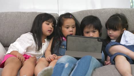 Gruppe-von-Kindern,-die-mit-digitalem-Tablet-zusammen-auf-dem-Sofa-zu-Hause-spielen,-und-lächelnd,-Kinder-auf-digitalem-Tablet-im-Wohnzimmer.