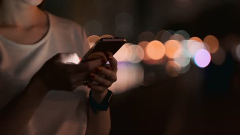 Close-up-de-un-teléfono-móvil-en-las-manos-de-una-chica-en-la-ciudad-por-la-noche