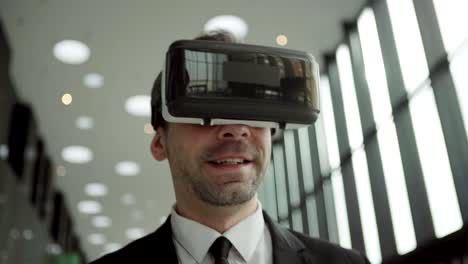 Close-up-shot-of-middle-aged-businessman-in-virtual-reality-headset-having-video-call-and-talking-while-walking-along-office-corridor