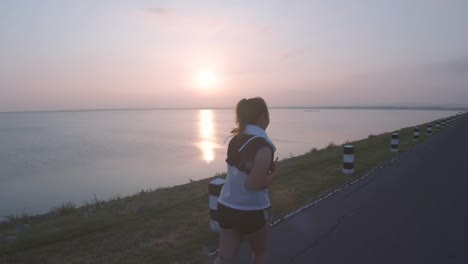 Asiatische-Frauen-joggen-in-der-Straße-am-frühen-Morgen-Sonnenlicht-am-Wasserspeicher-Pa-Sak-Jolasid-Dam.-Konzept-des-Gewichtsverlustes-mit-Bewegung-für-die-Gesundheit.-Langsame-Bewegung,-Rückansicht