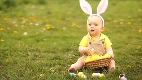 Adorable-bebé-en-un-disfraz-de-conejo-de-Pascua-recoge-los-huevos-de-Pascua-en-una-cesta-sentada-en-la-hierba-en-el-parque.-Picnic-de-primavera,-Feliz-familia-de-Pascua