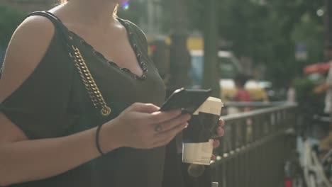 Joven-atractiva-chica-escribiendo-un-mensaje-de-texto-en-su-teléfono-inteligente-en-la-salida-del-metro-en-la-calle,-sosteniendo-su-café,-durante-el-verano-soleado-en-París.-Están-de-moda-y-fresco,-inclínate-hacia-abajo.-Pecas,-gafas-de-sol.