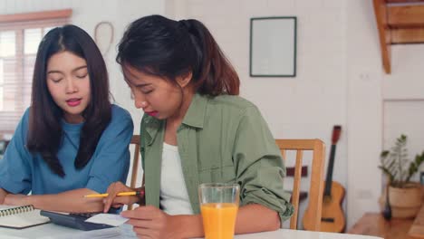 Business-Asian-Lesbian-couple-using-calculator-record-budget,-tax,-financial-document-on-laptop-working-in-kitchen.