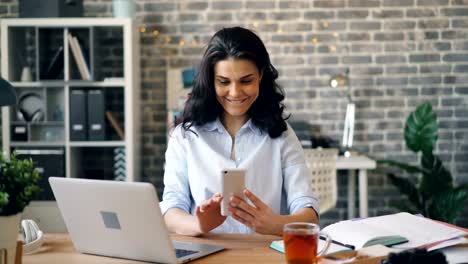 Mujer-con-teléfono-inteligente-disfrutando-de-las-redes-sociales-en-el-trabajo-tocando-la-pantalla-sonriendo