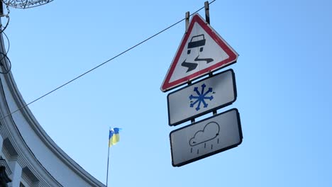 Verkehrsschilder,-die-auf-einem-Draht-unter-der-Straße-wehen---rutschige-Straße-bei-schneebedecktem-oder-regnerischem-Wetter