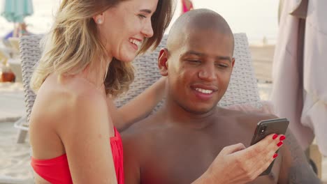 Charming-multiethnic-couple-laughing-watching-something-funny-on-smart-phone