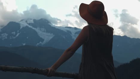 Back-view-of-hipster-girl-in-hat-excited-with-journey-to-mountains,-happy-young-woman-wanderlust-looking-alps-peaks-feeling-freedom-and-happiness-close-to-nature.