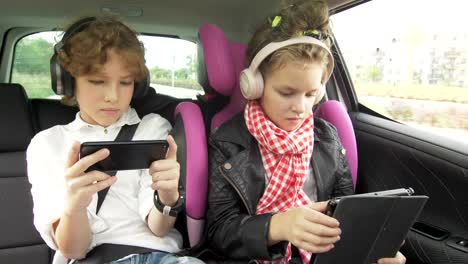 Junge-und-Mädchen-mit-Kopfhörern-Spielen-eines-Tablets-und-Smartphone-in-einem-Auto,-Kinder-mit-einem-Gerät-im-Auto.-Bruder-und-Schwester-reisen-zusammen