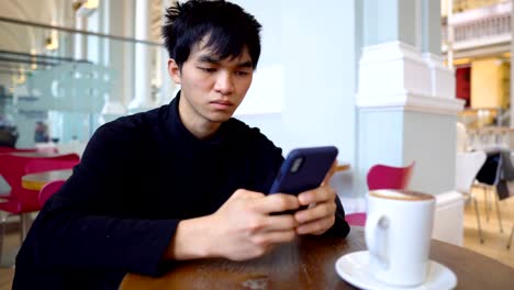 Joven-Asiático-Hombre-enviando-mensajes-de-texto-por-teléfono-mientras-está-sentado-en-la-cafetería