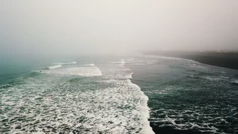 Aerial-view-of-ocean-shore-and-waves-with-surfers-in-fog