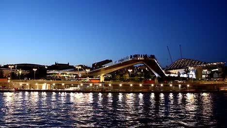 Schwimmende-Brücke-von-Zaryadye-Park-auf-Moskvoretskaya-Embankment-des-Flusses-Moskva-(und-touristisches-Vergnügungsboot)-bei-Nacht.-Moskau,-Russland.