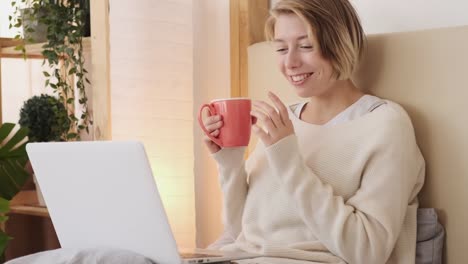 Happy-woman-video-chatting-using-laptop-in-bed