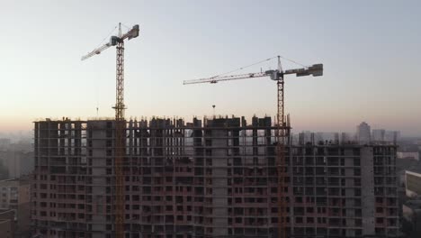 Aerial-Shot-of-the-Building-in-the-Process-of-Construction.-Labor-working-in-big-construction-site.-In-the-Background-Working-Crane-and-city