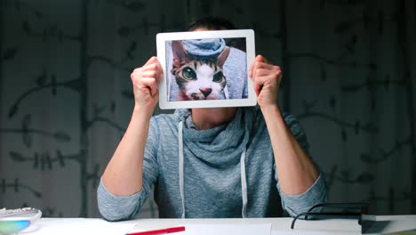 Ein-Mann-hält-eine-Tablette-mit-einer-Katze-in-den-Händen.