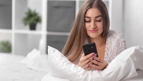 Porträt-schöne-Frau-in-Pyjamas-mit-Smartphone-auf-dem-Bett-liegen.-Nahaufnahme-auf-4k-RED-Kamera