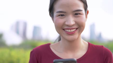 Nahaufnahme-Gesicht-der-asiatischen-Frau-mit-Smartphone.-Glückliches-weibliches-Gesicht-mit-weißen-Zähnen-hübsche-Gesicht-posiert-für-Nahaufnahme-Porträt-im-Freien.