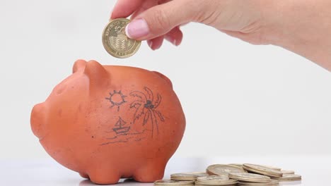 Woman-saving-money-into-a-traditional-clay-piggy-bank-for-holidays