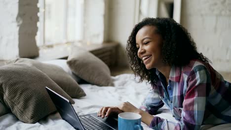 Lauging-rizado-afro-americano-niña-usando-laptop-para-compartir-redes-sociales-acostado-en-la-cama-en-casa