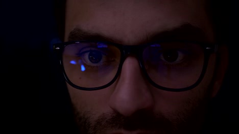 Portrait-Man-earns-bitcoins-on-his-bitcoin-farm.-Closeup-shot-of-boy-in-glasses-surfing-internet-at-night.-Close-up-of-young-man-reading-his-tablet-in-the-dark.-Black-background-in-focus.-Slow-Motion