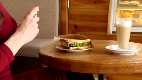 Moda-mujer-con-vestido-rojo-en-un-café-de-hacer-foto-de-alimentos-de-sandwich-con-cámara-de-teléfono-móvil-para-redes-sociales