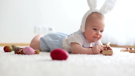 Niedlichen-Kleinkind-Kleinkind,-Baby-Boy,-im-sonnigen-Wohnzimmer-spielen-mit-Schokolade-Osterhasen-und-bunte-Ostereier