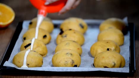 Rohe-ungebackenen-Brötchen.-Bereit,-hausgemachte-Ostern-traditionelle-Hot-Cross-Buns-auf-Backpapier-backen.-Weibliche-Hände-machen-ein-Kreuz.