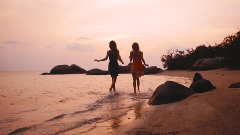 two-happy-girls-running-into-water-at-sunset-in-slow-motion