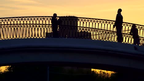 Silhouetten-von-Menschen,-die-Überquerung-des-Kanals-auf-eine-Bucklige-Brücke